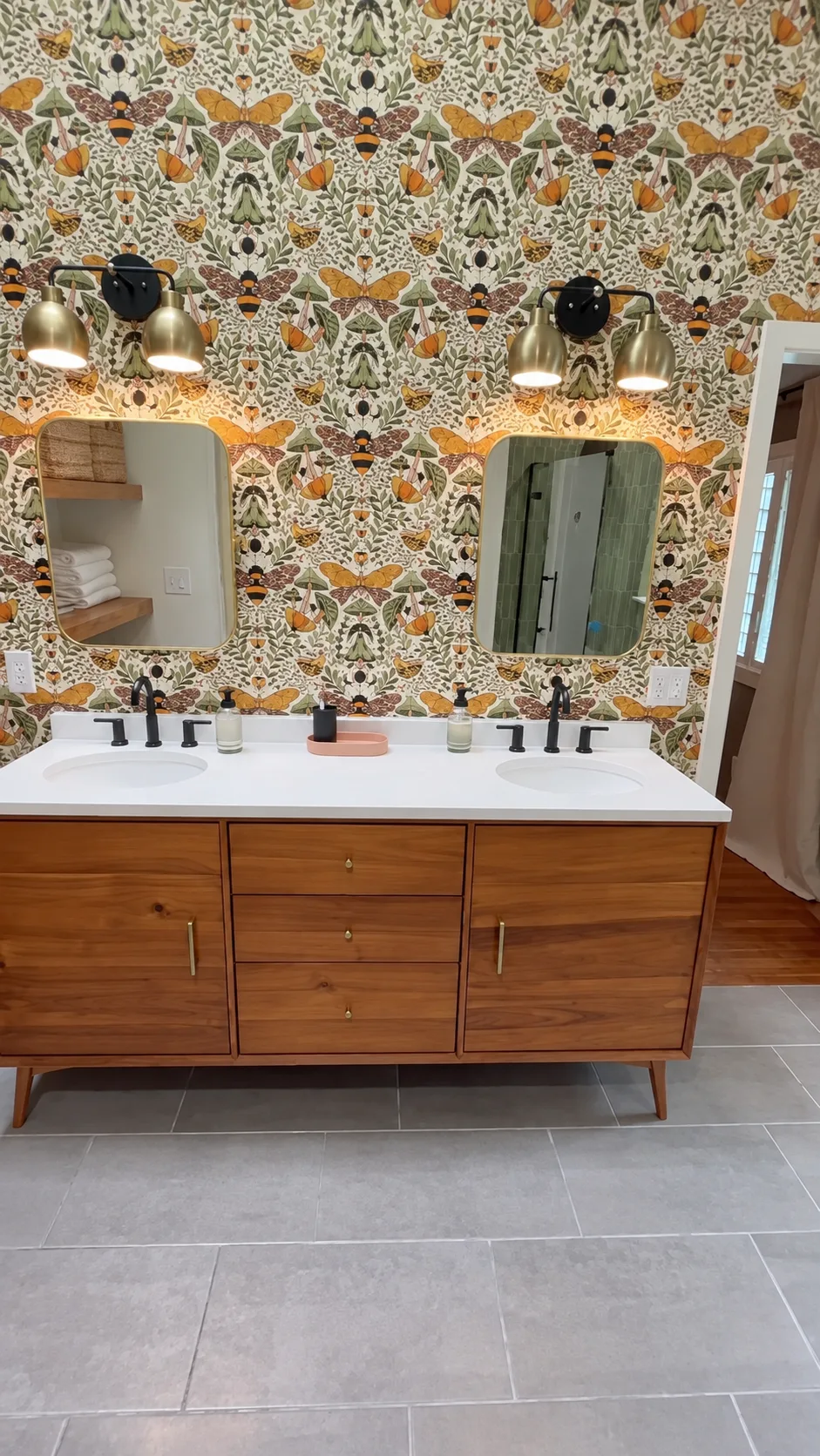 Cary bathroom double walnut vanity with patterned wallcovering, individual mirrors, and warm sconces